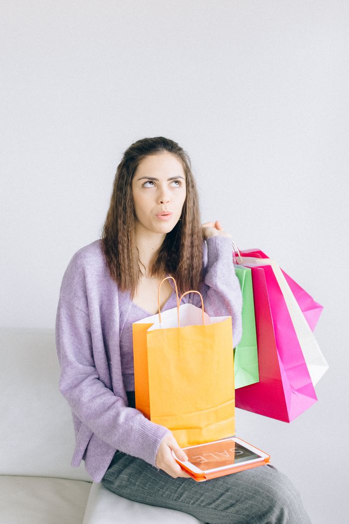 who-we-are Young woman holding shopping bags and digital tablet indoors, pondering a purchase.