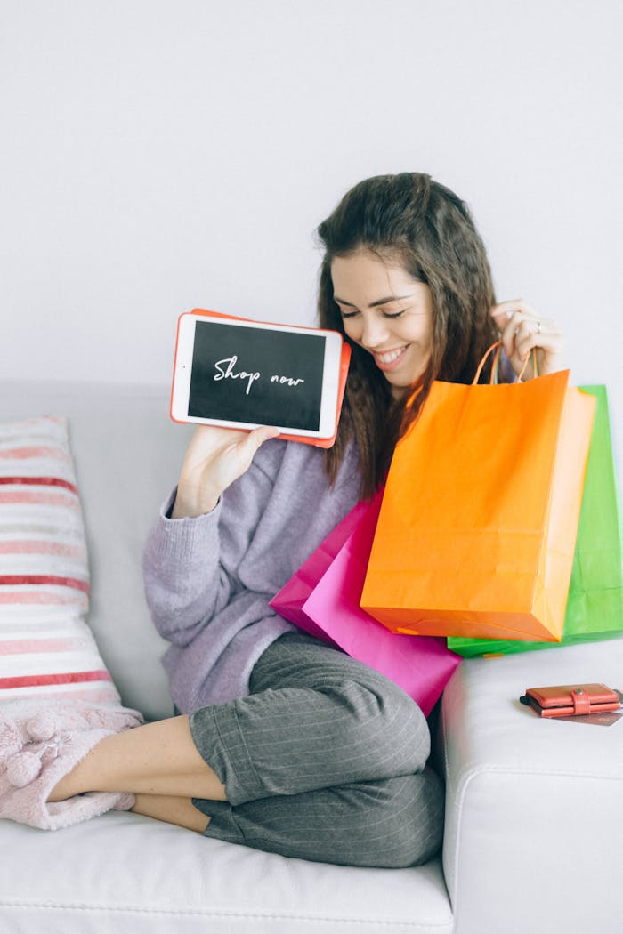 our-journey-02 Woman holding a tablet and colorful shopping bags on a sofa, enjoying online shopping at home.