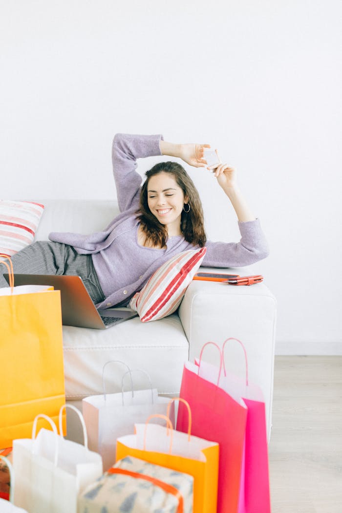 Woman comfortably shopping online with multiple bags around her.