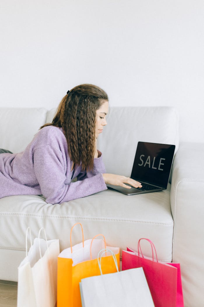 our-journey-03 Woman browsing online sale while lying on a couch with shopping bags nearby.