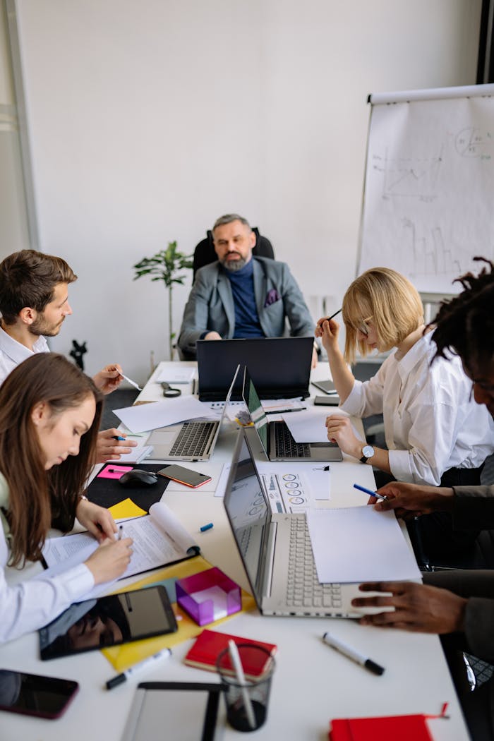 Group of colleagues brainstorming and planning in a modern office with laptops and documents.